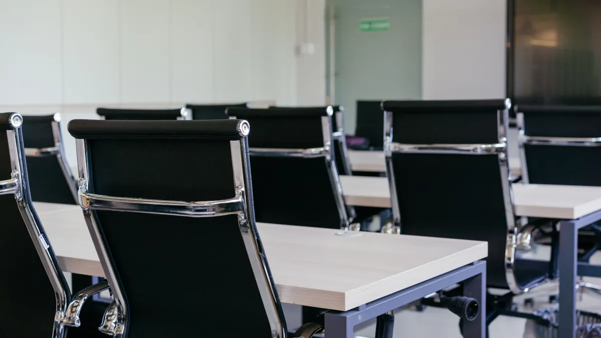 Salle de conférence moderne avec chaises noires et bureaux blancs.